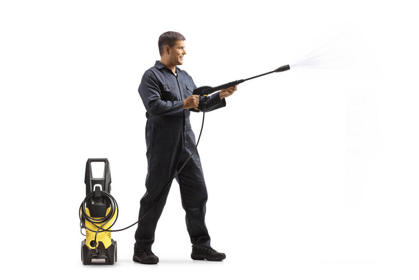 Full length profile shot of a male worker in a uniform using a pressure washer machine isolated on white background - Foto, Bild