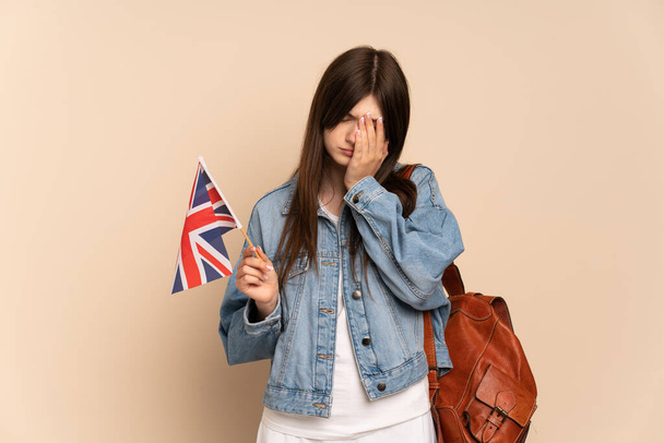 Young Ukrainian girl holding an United Kingdom flag isolated on beige background with tired and sick expression - 写真・画像