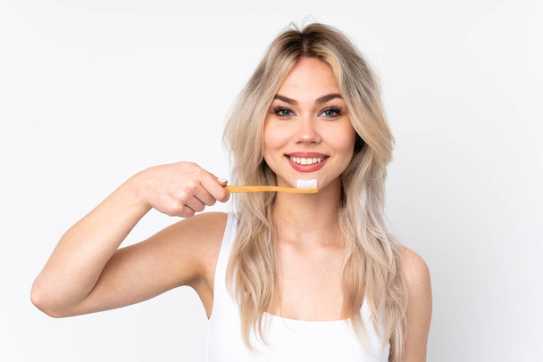 Teenager blonde girl over isolated white background with a toothbrush and happy expression - Photo, image
