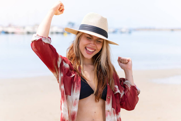 Young pretty woman in summer holidays at beach celebrating a victory - Фото, изображение
