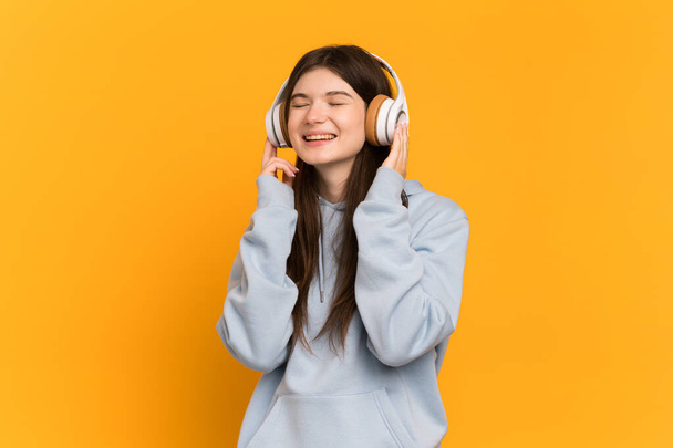 Menina ucraniana jovem isolado no fundo amarelo ouvir música e canto - Foto, Imagem