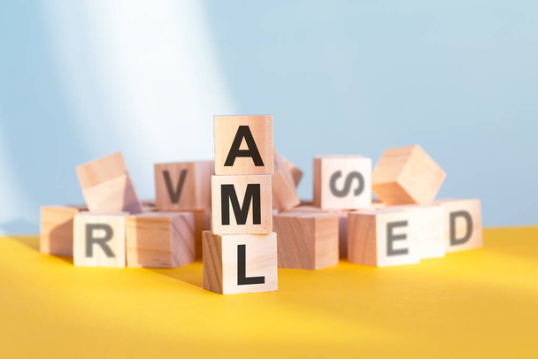 cubos de madeira com letras AML dispostos em uma pirâmide vertical, fundo cinza e amarelo, conceito de negócio. AML - abreviação de ANTI-MONEY LAUNDERING - Foto, Imagem