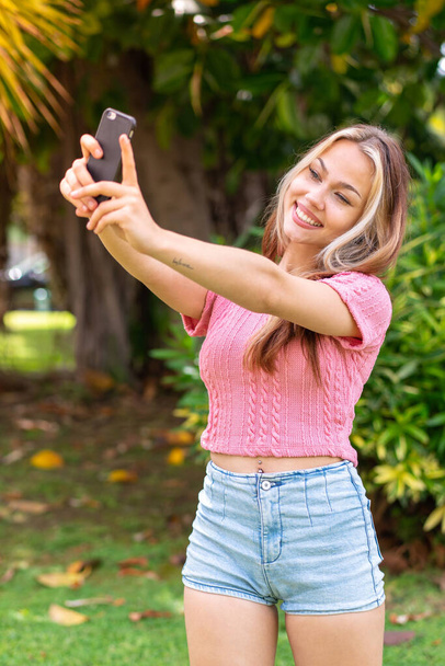 Joven mujer bonita al aire libre usando el teléfono móvil y haciendo una selfie - Foto, Imagen