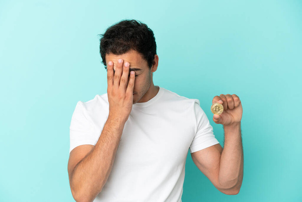 Young man holding a Bitcoin over isolated blue background with tired and sick expression - Φωτογραφία, εικόνα