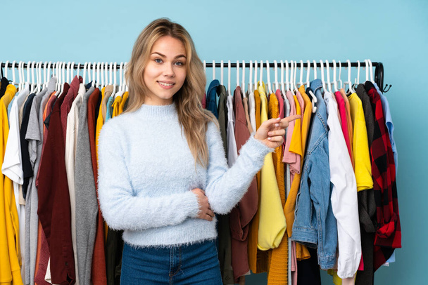 Teenager Russian girl buying some clothes isolated on blue background pointing finger to the side - Foto, immagini