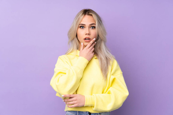 Teenager girl wearing a yellow sweatshirt over isolated purple background surprised and shocked while looking right - Foto, imagen