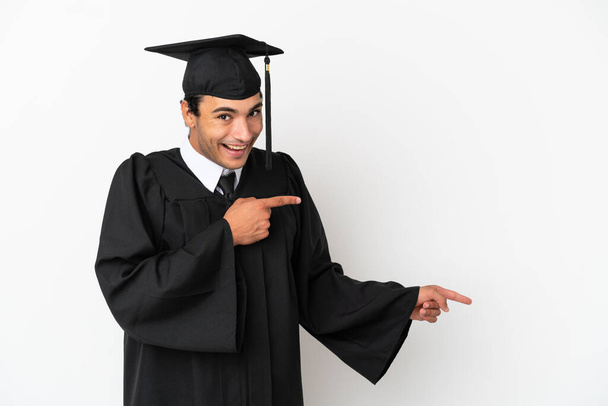 Jeune diplômé universitaire sur fond blanc isolé surpris et pointant côté - Photo, image