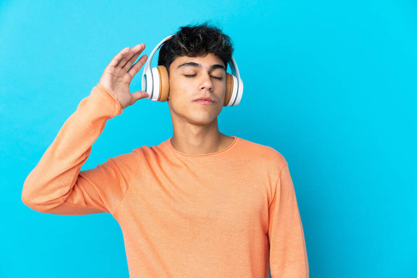 Jongeman over geïsoleerde blauwe achtergrond luisteren muziek en dansen - Foto, afbeelding