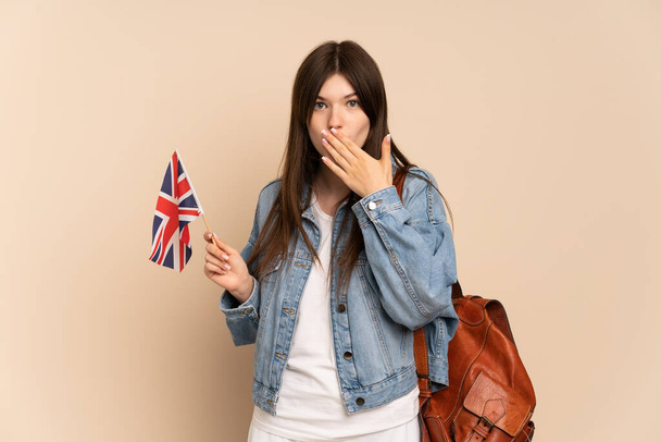 Young Ukrainian girl holding an United Kingdom flag isolated on beige background happy and smiling covering mouth with hand - Photo, Image
