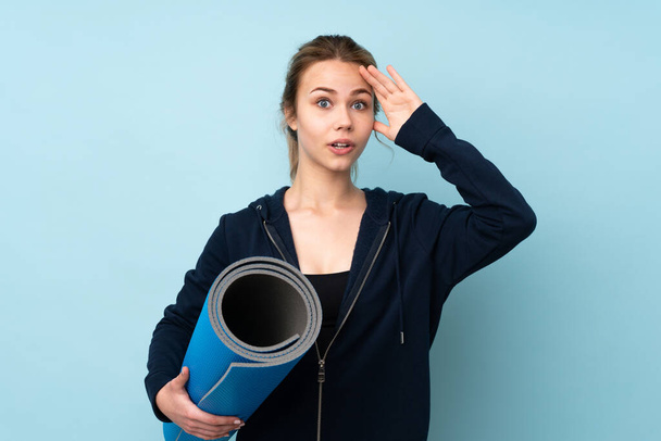 Teenager Russian girl holding mat isolated on blue background with surprise expression - 写真・画像