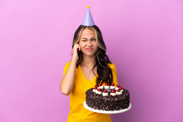 Adolescente rusa chica sosteniendo pastel de cumpleaños aislado sobre fondo púrpura frustrado y cubriendo las orejas - Foto, imagen