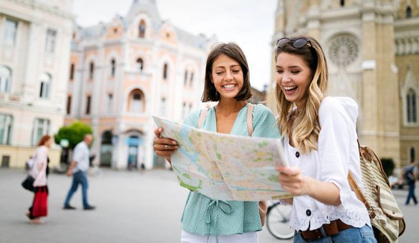 Fun, friends, travel and tourism concept. Beautiful happy women looking for direction in the city - Foto, Bild