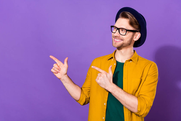 Photo of young man happy positive smile look indicate fingers empty space select suggest promo isolated over purple color background - Foto, Imagen