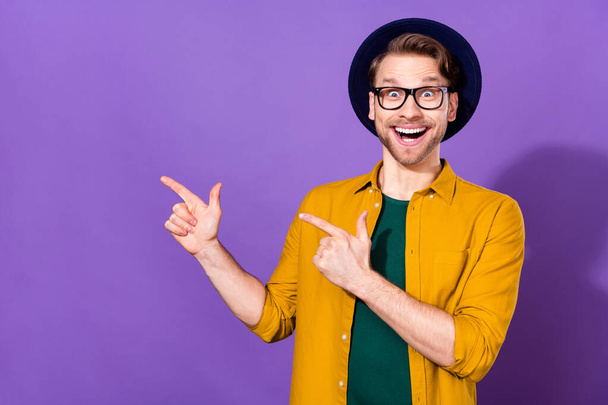 若い興奮した男の写真幸せな正の笑顔ポイント指空のスペース選択広告は紫の色の背景に孤立 - 写真・画像