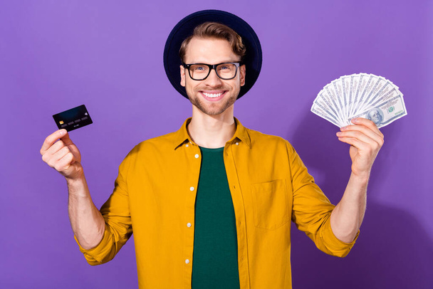 Photo of young guy happy positive smile hold cash money dollars bank card pay isolated over violet color background - Фото, зображення