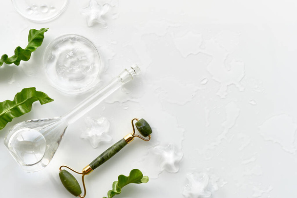 Moisturizer, green jade face roller with ice pieces. Exotic fern leaves. Minimal flat lay on off white background, copy-space . Facial massage, handmade cosmetics, top view with text place. - Fotografie, Obrázek