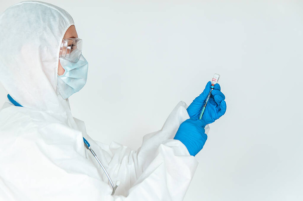 Doctor or nurse in a protective suit holds a syringe and a covid 19 vaccine - Fotó, kép