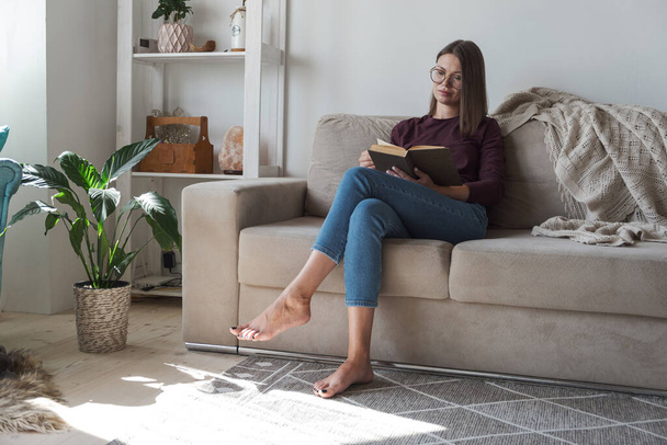 Woman reading book and relaxing sitting in sofa at home - Foto, Imagem