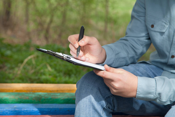 Caucasian man writes with a pen on documents. Outdoors. - 写真・画像