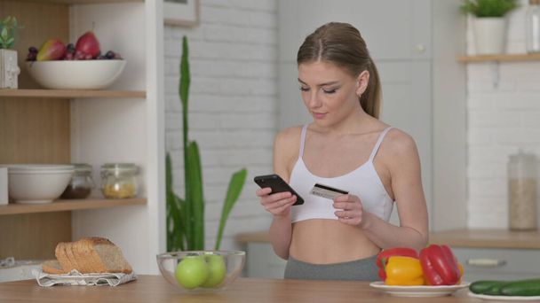 Woman Doing Online Shopping on Smartphone in Kitchen - Foto, afbeelding