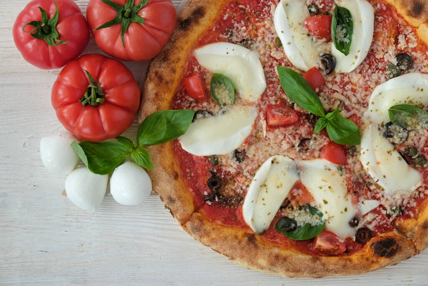 Cropped shot of oven baked pizza with buffalo mozzarella, parmigiano-reggiano cheese, basil and anchovies. Traditional italian dish on wood textured table background. Close up, copy space, top view. - Fotoğraf, Görsel