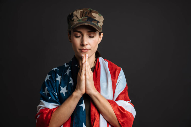 Calm soldier woman with american flag holding palms together isolated over black background - Foto, Imagen