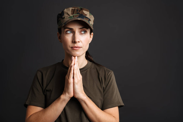 Calm beautiful soldier woman holding palms together isolated over black background - Foto, immagini