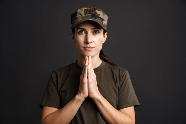 Calm beautiful soldier woman holding palms together isolated over black background - Foto, afbeelding
