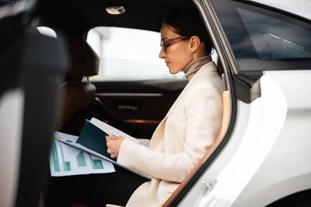 Beautiful focused businesswoman working with papers while sitting in car - Φωτογραφία, εικόνα