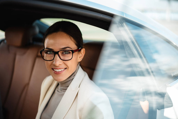 Hermosa mujer de negocios feliz en anteojos sonriendo mientras está sentado en el coche - Foto, imagen