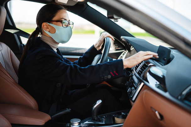 Beautiful focused businesswoman in face mask using navigator while driving car - Foto, afbeelding