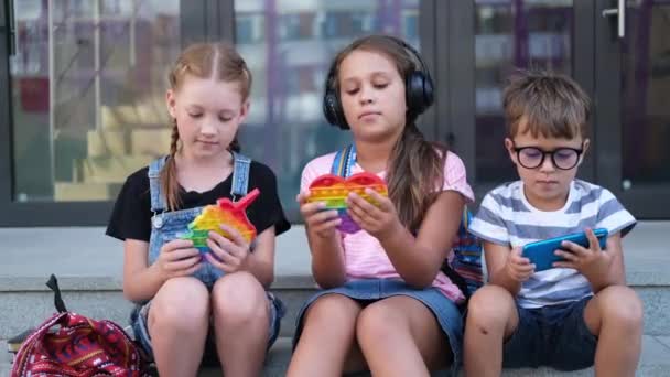  Tres niños con mochila sentarse y jugar popit y teléfono - Imágenes, Vídeo