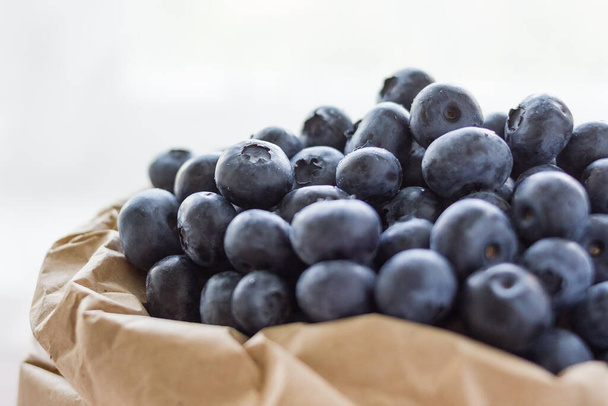 A lot of beautiful juicy fresh summer blueberries in a brown bag on a light background - Foto, imagen