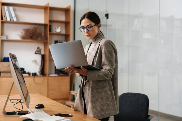Focused charming woman in eyeglasses working with computer and laptop at office - Фото, изображение