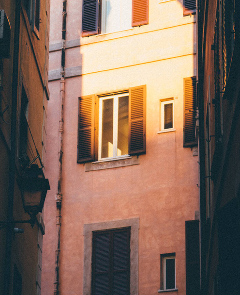 A vertical shot of golden sunlight shining on a window with open shutters in the streets of Rome, Italy - Фото, зображення