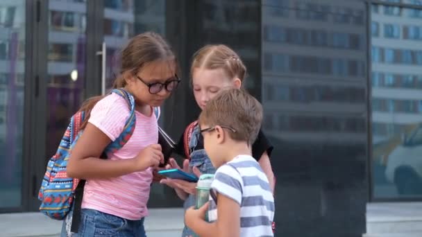  Tres niños con la mochila de pie y hablar juntos y jugar teléfono - Imágenes, Vídeo