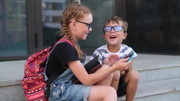 Due bambini in occhiali con libri e zaino parlano al telefono - Filmati, video
