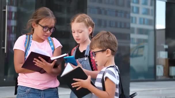  Drie kinderen met rugzak staan en lezen boek met telefoon - Video