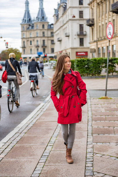 Asian woman walking in red fashion trench coat relaxing outside in Copenhagen city street, Denmark. Europe travel tourism tourist enjoying european lifestyle. - Foto, imagen