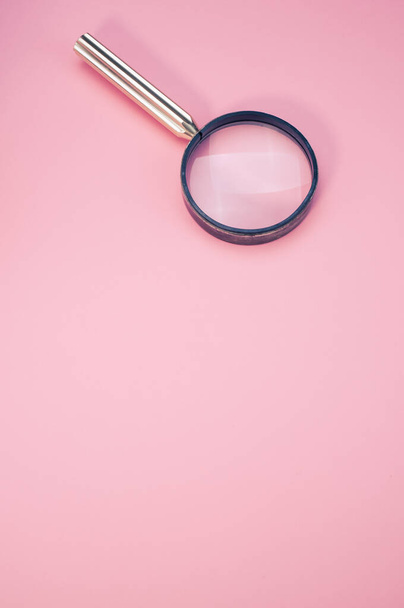 A vertical closeup of a magnifier on pink background. - Foto, Bild