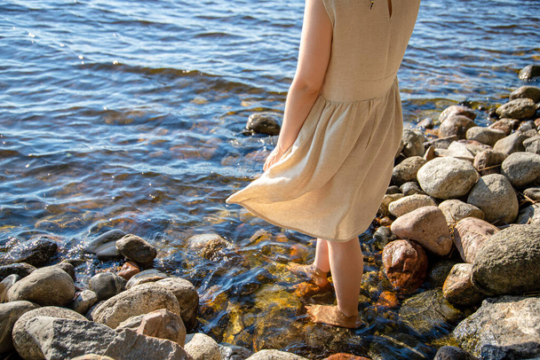 A young female in a dress standing on a rocky seashore - Фото, зображення