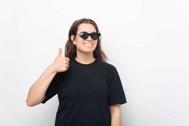 Гарна фотографія молодої жінки, яка посміхається в камеру з сонячними окулярами, показує великий палець вгору
 . - Фото, зображення