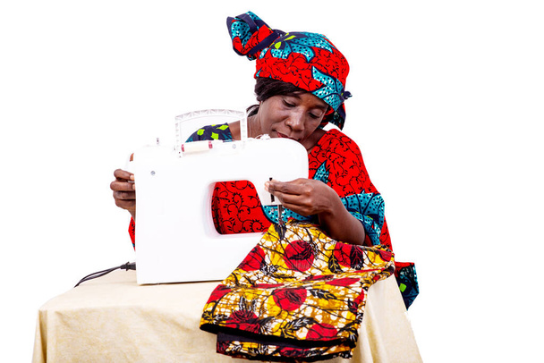uma costureira em vestido tradicional sentado em sua oficina costurar uma saia. - Foto, Imagem