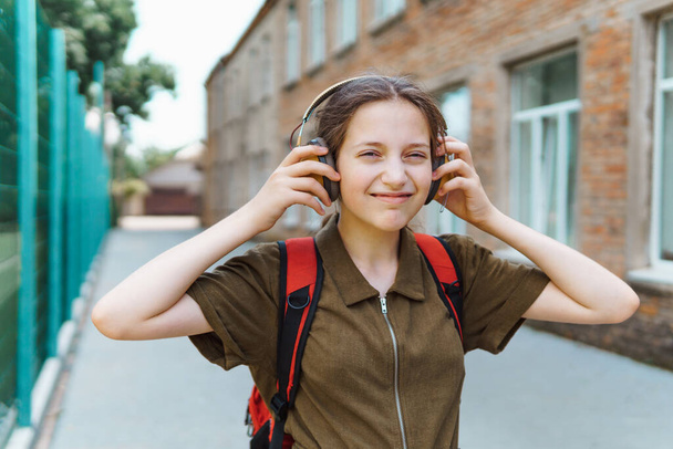 Szczęśliwa uczennica w drodze do szkoły. Słucha muzyki przez słuchawki. Edukacja i powrót do koncepcji szkoły - Zdjęcie, obraz