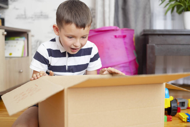 Мальчик распаковывает картонную коробку (подарочную коробку или посылку) дома. Концепция доставки и обслуживания. Интернет-магазины. - Фото, изображение