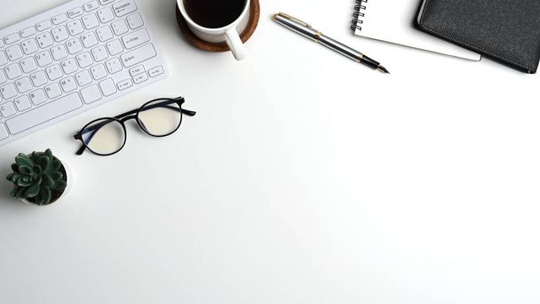 Pohled shora na bílý kancelářský stůl s notebookem, šálkem kávy, brýlemi, klávesnicí a kopírovacím prostorem. - Fotografie, Obrázek