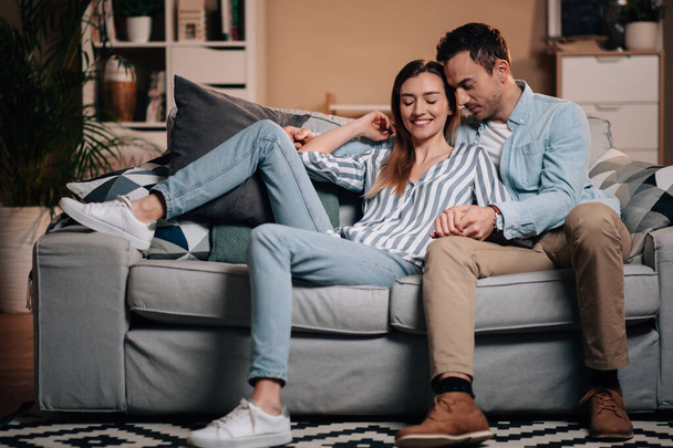 Retrato de una joven pareja con ropa casual en el sofá abrazándose - Foto, Imagen