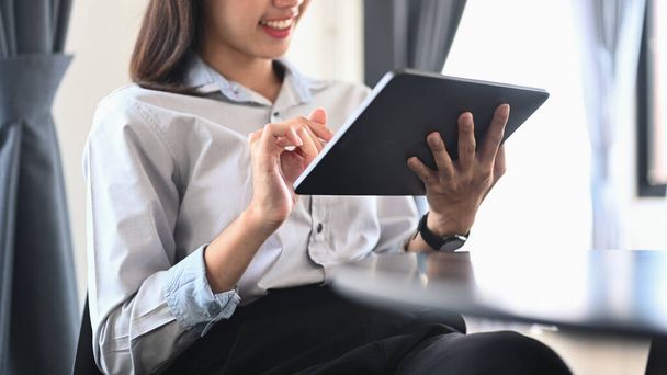 Cropped shot of smiling young woman employee sitting in office and using digital tablet. - Foto, Imagen
