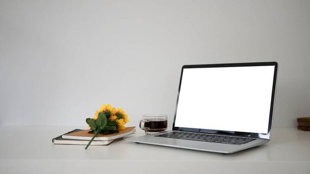 Computer-Laptop mit leerem Bildschirm, Kaffeetasse, Notizbuch auf weißem Tisch. - Foto, Bild
