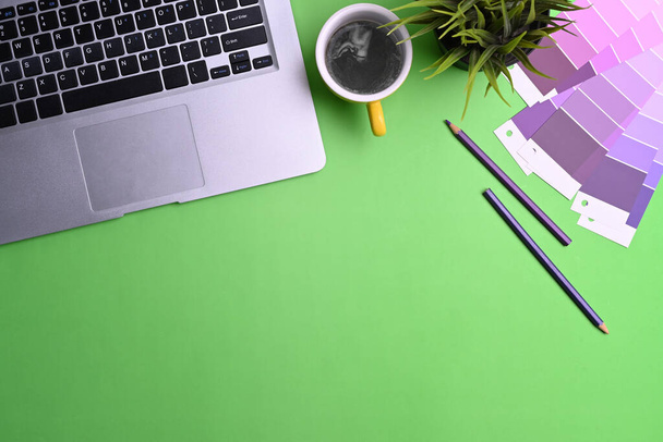 Bovenaanzicht van grafisch ontwerper werkruimte met computer laptop, kleurstalen, koffiebeker en notebook op groene achtergrond. - Foto, afbeelding